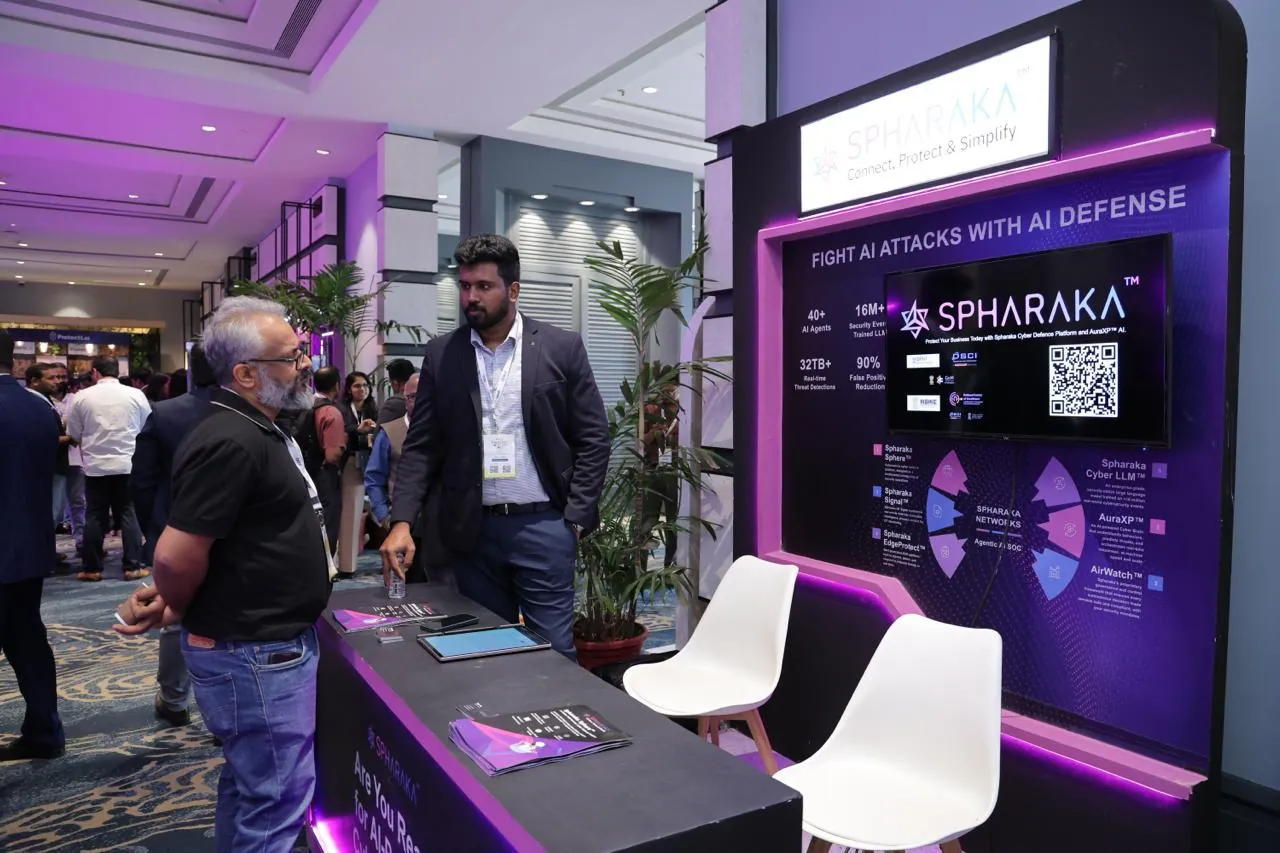 The Spharaka exhibition stand, showing the platform overview screen and the headline Fight AI attacks with AI defense, with a visitor in conversation.