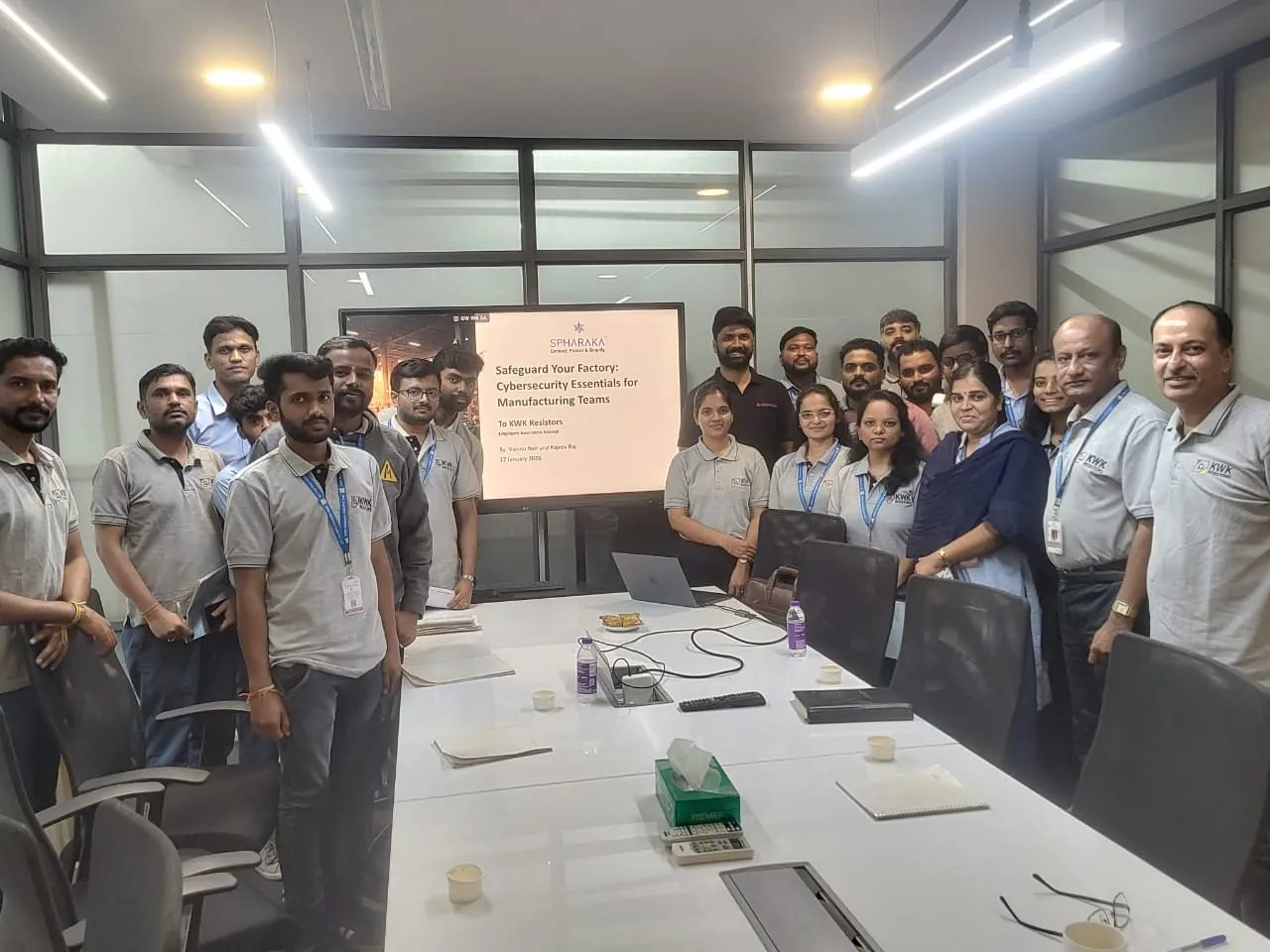 The KWK Resistors team photographed in their meeting room after a Spharaka employee awareness session, with the session title slide on the screen behind them.